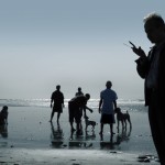 Man with mobile phone at beach with people and dogs in background