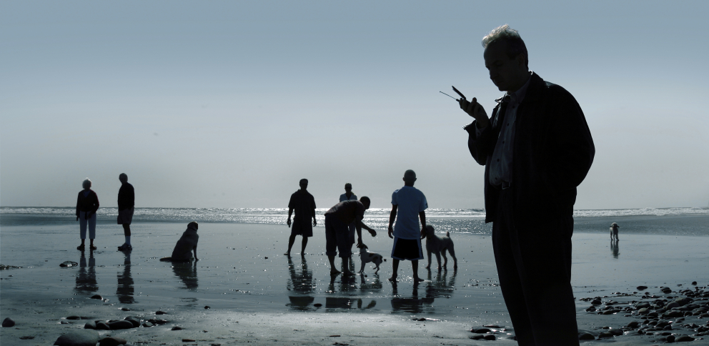 Man with mobile phone at beach with people and dogs in background